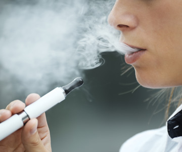 A woman holding a vaping device exhales.