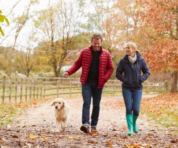 Man and woman walking with a dog on a path with fall leaves.