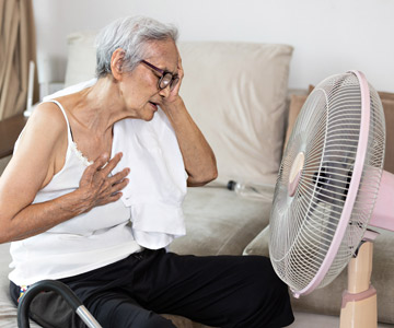 Woman cooling herself with fan on a hot day. Extreme Weather support is available for qualified Medicaid members.
