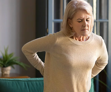 Woman with arms on back grimacing with pain