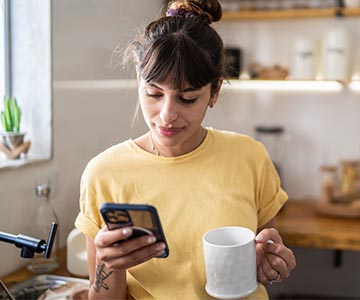 Woman looking at phone with cup of coffee in hand