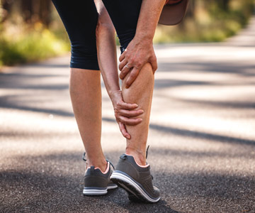 Person in running shoes stops to grab her calf that is cramping.