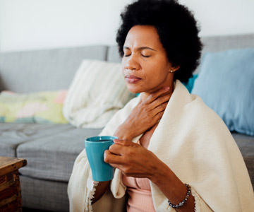 A woman closing her eyes with a sore throat and blanket around her shoulders.