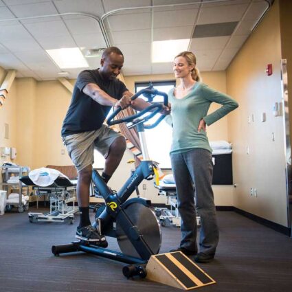 Therapist watches other on stationary bike.