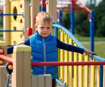 A young boy alone on a playground structure looks hesitant.