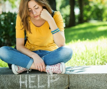 Woman sits cross legged on sidewalk curb with her chin on her hand