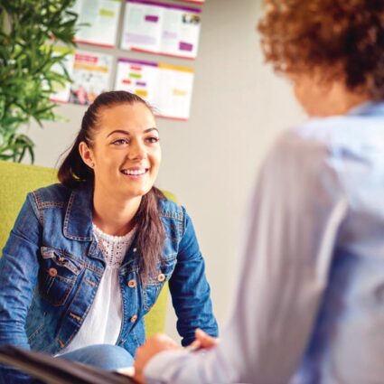 Smiling young woman converses with other.